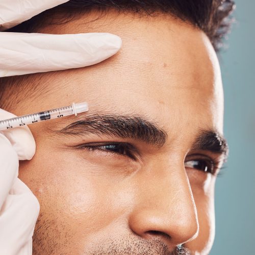 Beauty, botox and eyebrow with a man in studio on a gray background for a plastic surgery injection. Hands, skincare and syringe with a young male person indoor for an antiaging facial filler closeup Beauty, botox and eyebrow with a man in studio on a gray background for a plastic surgery injection. Hands, skincare and syringe with a young male person indoor for an antiaging facial filler closeup.